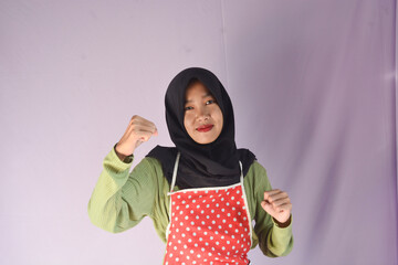 Portrait of an Indonesian woman standing confidently wearing an apron and carrying cooking utensils on an isolated background, Copy space