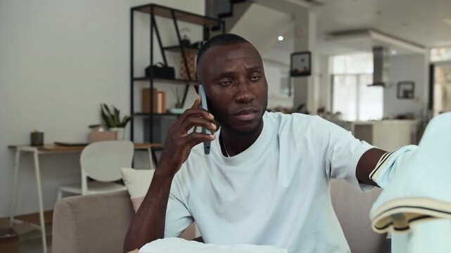 Medium shot of black male sad customer calling support on cellphone while getting wrong T-shirt from online store