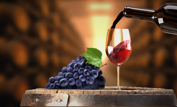 Vin rouge vers&eacute; d'une bouteille dans un verre &agrave; vin. Grappe de raisin noir pos&eacute; sur un tonneau de vin dans une cave. Appel &agrave; la d&eacute;gustation.