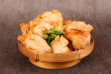 Close up of fried food served in a woven bamboo container on a dark background.
