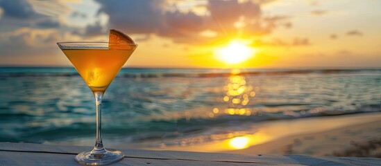 A cocktail glass with a beach view in the background during a sunset highlighting a serene atmosphere with copy space image