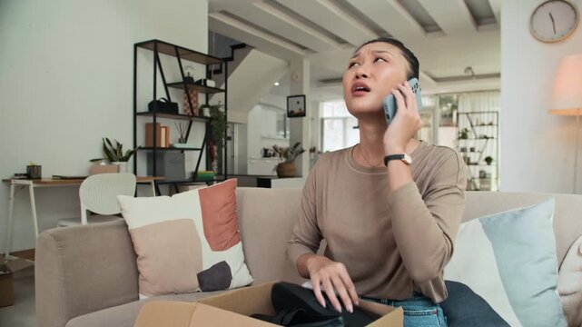 Medium shot of young female Asian client asking delivery service about wrong pair of shoes in her parcel at home