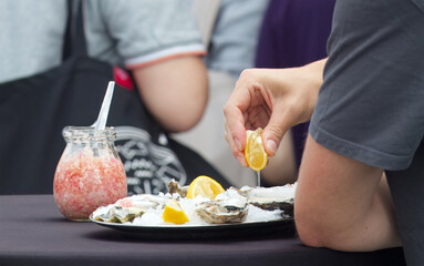 Midsection of man holding slice of lemon and eating fresh mussels from metal tray with ice chips in the farmers market.