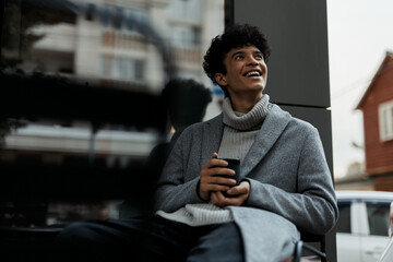 Young man sitting in chair with coffee, smiling at camera