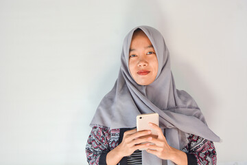 Portrait of an Asian woman holding a smartphone while smiling at the camera and raising her hand showing an okay gesture. on an isolated background