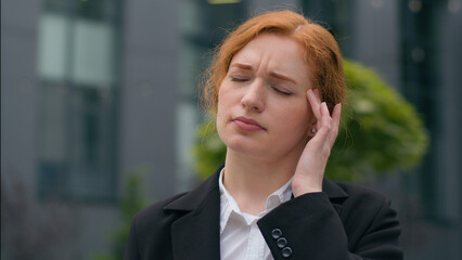 Fototapeta premium Tired worried upset young ginger Caucasian girl woman female sad businesswoman student elegant formal suit suffering painful headache anxiety pressure touching head pain outdoors downtown city street