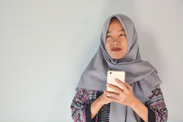 Portrait of an Asian woman holding a smartphone while smiling at the camera and raising her hand showing an okay gesture. on an isolated background