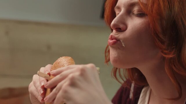 Close up hungry Caucasian pleased woman female client girl consumer with closed eyes chewing burger eat tasty hamburger bite cheeseburger enjoying taste indoor. Overeating healthcare unhealthy eating