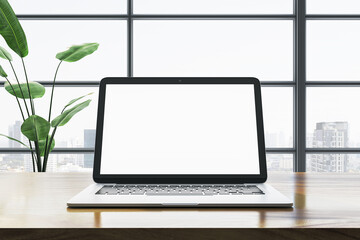 Fototapeta premium Modern laptop with blank screen on wooden desk in office with city view. 3D Rendering