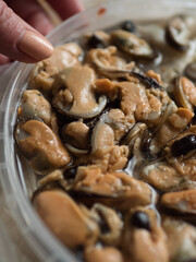 Vertical Close Up shot of a Woman’s Hand Touching a Plastic Containers with Marinated Mussels on Polyethylene Surface.