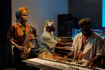 Musicians composing music in recording studio. One performer playing saxophone while another...