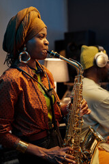 African American woman wearing headwrap playing saxophone in indoor setting during cozy scene with...