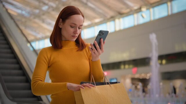 Serious confused Caucasian business woman female girl tourist customer businesswoman holding mobile phone device internet store app searching in paper bags card money buy online indoors shopping mall