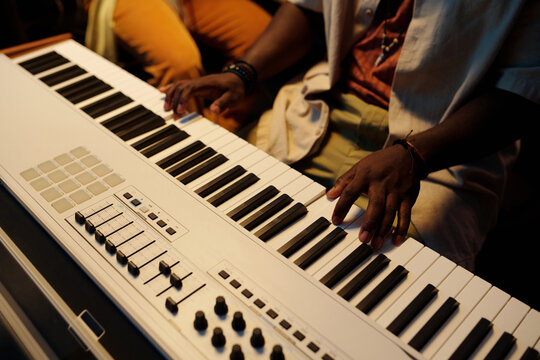 Person playing keyboard with hands on keyboard and adjustments on MIDI controller in music studio. Capturing creativity through musical performance
