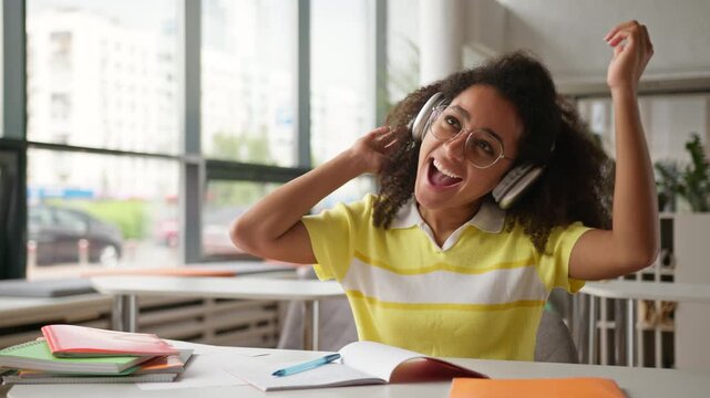 Happy funny dancing moving dance African American girl female student business woman listen music in headphones enjoy audio wireless earphones in cafe school university library college studying pause