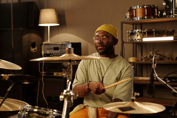 Drummer playing drums in cozy music studio filled with various instruments and recording equipment using drumsticks Holding a focused and concentrated expression while performing
