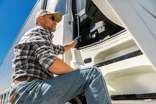 Trucker in Sunglasses Climbing Into a Modern Semi Truck During a Sunny Day