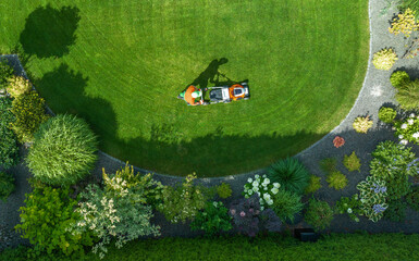 Person Mowing a Lush Green Lawn Surrounded by Vibrant Flowers in a Residential Garden