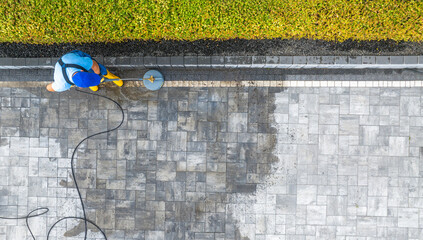 Worker Cleaning a Stone Patio With a Pressure Washer in a Residential Yard