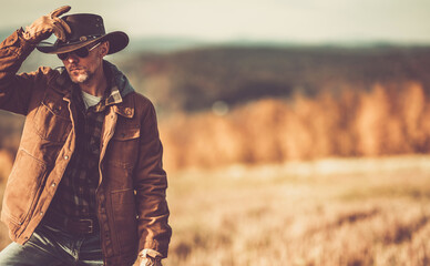 Man in a Cowboy Hat Poses Thoughtfully in a Golden Autumn Landscape During Sunset
