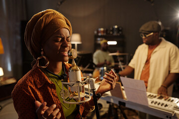 Group of musicians rehearsing in music studio with vintage microphone and various instruments, including keyboard and drums, creating dynamic and collaborative atmosphere