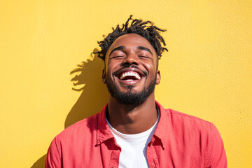 Fototapeta premium Black Man in Red Shirt and White T-Shirt, Laughing Joyfully on a Sunny Day, Close-Up Portrait with Sunlight and Yellow Wall Backdrop 