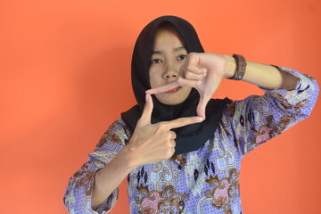 Fototapeta premium Portrait of Asian Muslim woman in hijab with hand gestures above forming a photo frame
