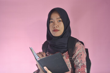 Portrait of an Indonesian schoolgirl wearing a bag on her back and carrying a book in her hand