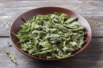 Dried mint leaves in a brown ceramic bowl on a wooden table, close up