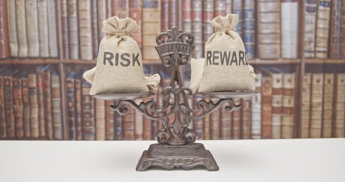 Risk reward ratio / risk management concept : Risk and reward bags on a balance scale in equal position, depicting investors use a risk reward ratio to compare the expected return of an investment.