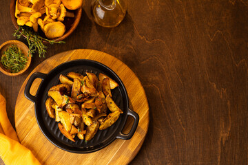 Chanterelle mushrooms fried in cast iron frying pan, herbs for roasted chanterelles thyme, oil and cloth. Raw chanterelles on a dark brown background of wooden table.