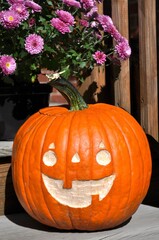 Obraz premium Close up of happy hand carved orange pumpkin and purple flowers on wooden stairs.