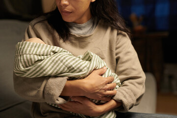 A mother gently cradling her newborn baby wrapped in striped blanket while sitting on couch, with soft lighting highlighting a serene scene