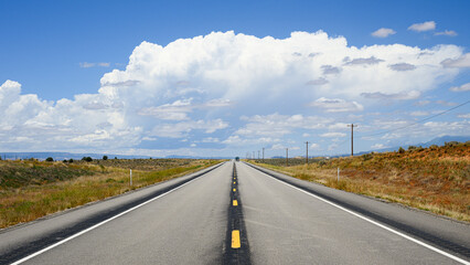 Two lane road passing open high desert towards large white cloud