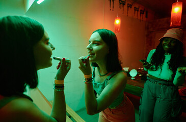Happy young brunette woman in denim tanktop and jeans standing in front of mirror in lavatory and...