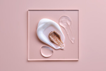 Textures of different cosmetic products on a pink background on a square transparent stand.
