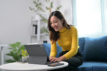 Young Woman Working on Laptop at Home, Smiling and Engaged in a Bright Modern Living Room Setting