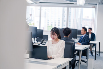 オフィスで笑顔でデスクワークをする若い女性