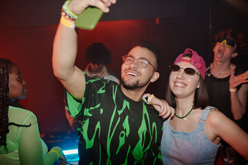 Happy young intercultural couple in trendy apparel looking at smartphone camera with toothy smiles...