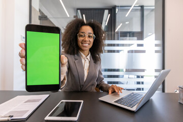 Portrait of a smiling young African-American businesswoman sitting in the office at a desk with a...