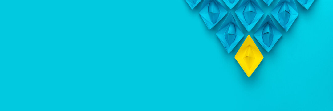 Yellow paper ship ahead of blue ones leadership concept over blue background. Top view of race with yellow winning paper ship metaphor. Minimalist conceptual image of leadership