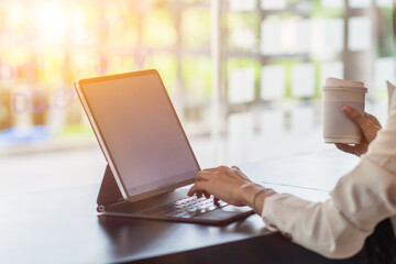 An Asian businesswoman holds a cup of coffee in her hand and drank while checking her computer online as she is starting a business that can order and check from anywhere online.