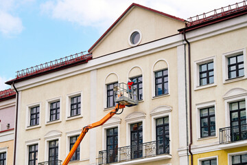 Worker washing windows with crane bucket lift. Laborer on cherry picker washing windows at height. Industrial alpinist wash windows, facade maintenance. Cleanup service