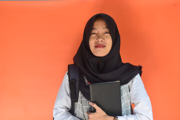 Portrait of a muslim schoolgirl carrying books in her hands and wearing a black backpack on an isolated background