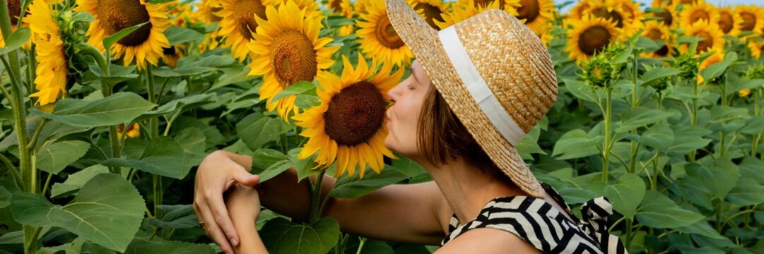 A Caucasian woman enjoys a summer day in a sunflower field, emphasizing nature appreciation and relaxation during harvest season