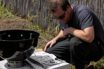 Caucasian man studying instructions while assembling a barbecue grill, symbolizing summer outdoor...