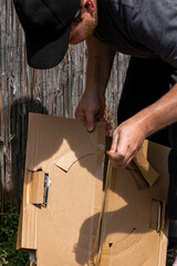 Caucasian man wearing a black cap and working on assembling a cardboard box outside, related to moving or shipping