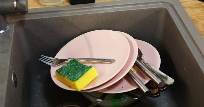 Dirty dishes placed in kitchen sink with food leftovers in clogged waste strainer. Task of cleaning up after meals requires timely action to keep cleanliness