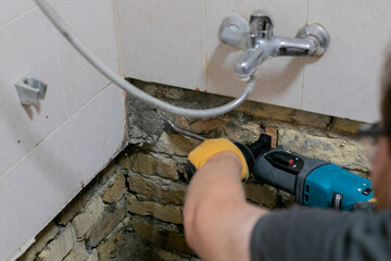 A person using a power tool to repair a damaged bathroom wall, addressing home maintenance and plumbing issues