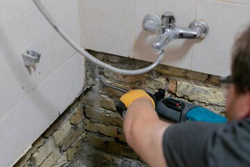 A man repairing water damage in bathroom tiles with a power tool, addressing home renovation and...